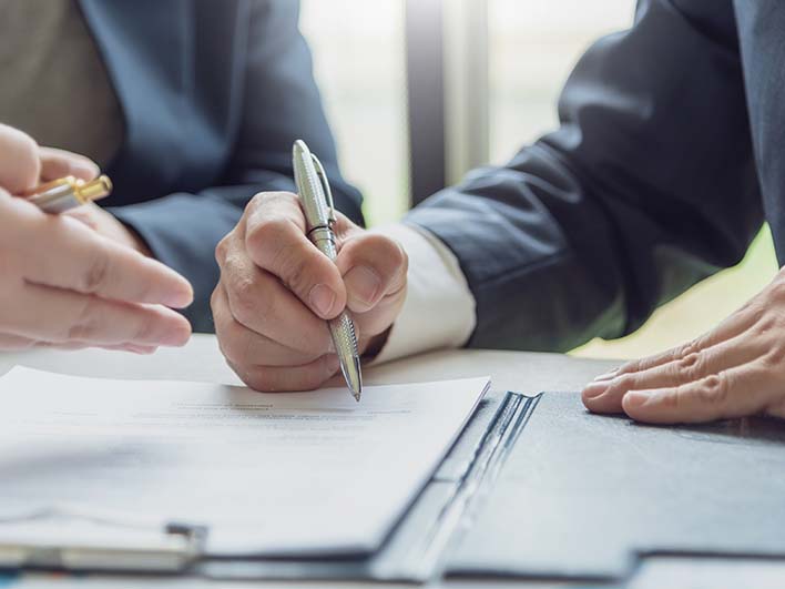 Close up of men in suits with pens signing papers