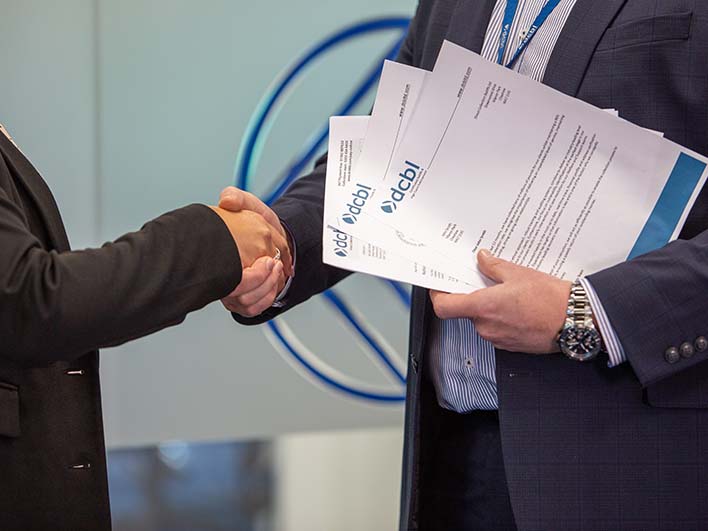 Close up of man and woman shaking hands with DCBL papers